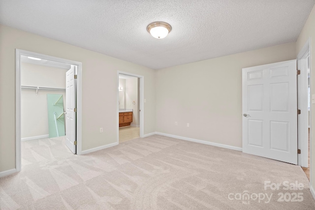 unfurnished bedroom with a textured ceiling, light colored carpet, baseboards, a closet, and a spacious closet