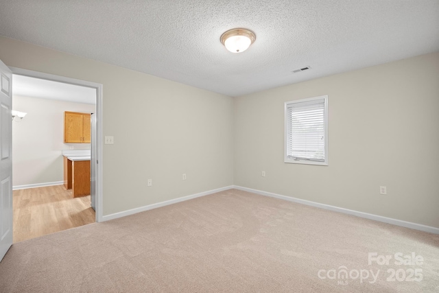 spare room featuring baseboards, a textured ceiling, and light colored carpet