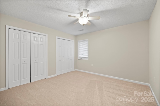 unfurnished bedroom with a textured ceiling, visible vents, light colored carpet, baseboards, and two closets