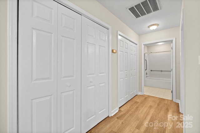 corridor featuring light wood-style floors, baseboards, and visible vents