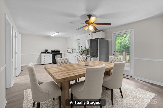 dining area featuring light wood-style flooring, ceiling fan, and wainscoting