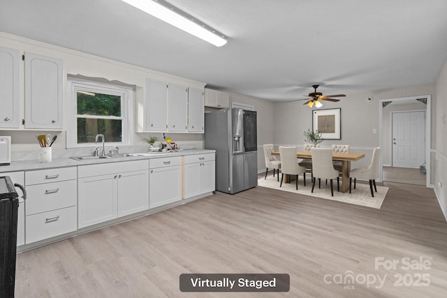 kitchen featuring a sink, stainless steel fridge, light countertops, and white cabinetry