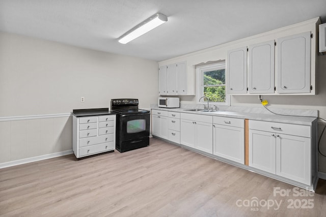 kitchen featuring electric range, white microwave, a sink, light wood-style floors, and white cabinetry