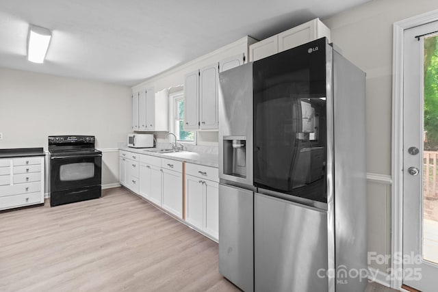 kitchen with stainless steel refrigerator with ice dispenser, electric range, white microwave, a sink, and white cabinetry