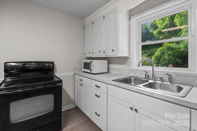 kitchen with black range with electric stovetop, white microwave, a sink, white cabinets, and light countertops