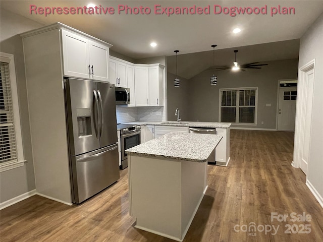 kitchen featuring appliances with stainless steel finishes, wood finished floors, a sink, a peninsula, and lofted ceiling