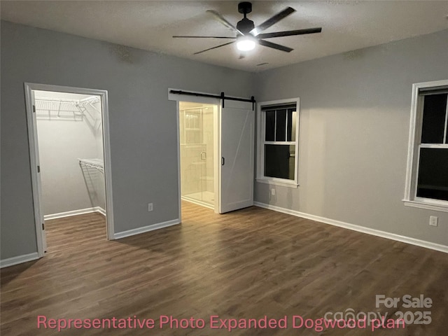 unfurnished bedroom featuring baseboards, ensuite bathroom, a walk in closet, dark wood-style floors, and a barn door