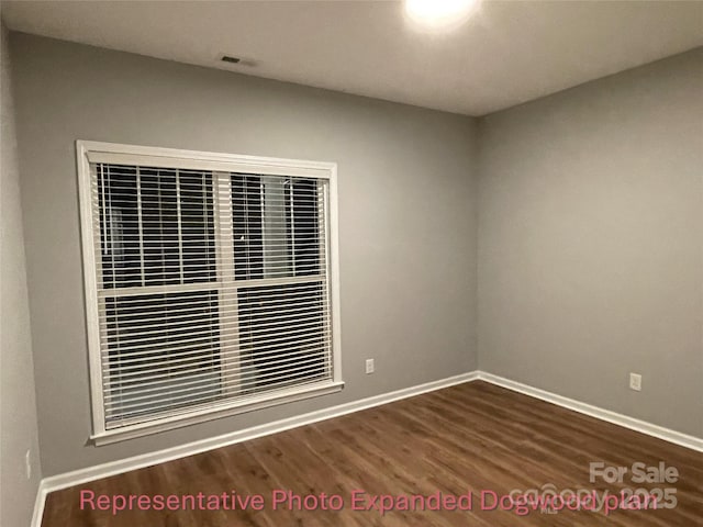 unfurnished room featuring baseboards, visible vents, and wood finished floors