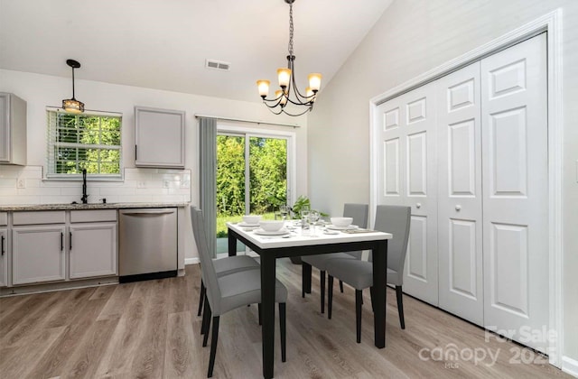 dining space with visible vents, light wood finished floors, a notable chandelier, and vaulted ceiling