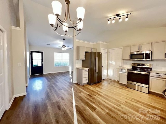 kitchen with appliances with stainless steel finishes, vaulted ceiling, wood finished floors, baseboards, and a notable chandelier