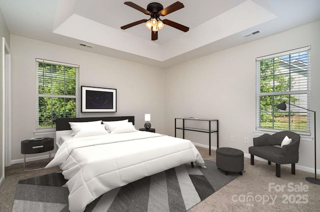carpeted bedroom featuring visible vents, baseboards, ceiling fan, and a tray ceiling