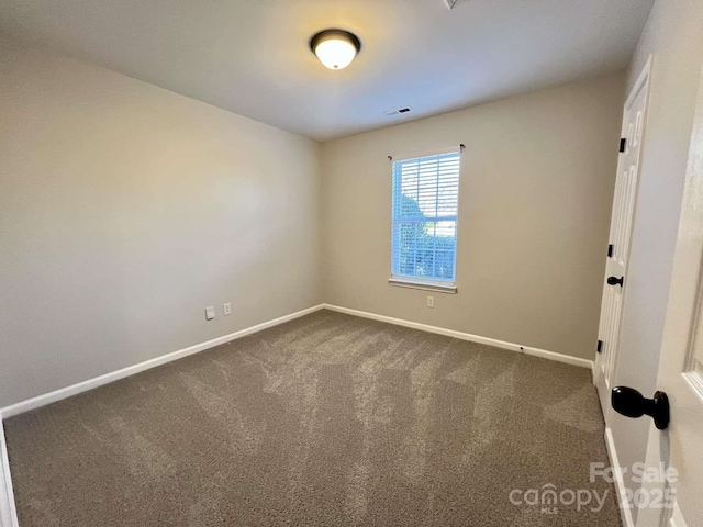 spare room featuring baseboards, visible vents, and dark colored carpet