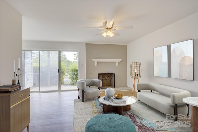 living area featuring a ceiling fan, wood finished floors, and a brick fireplace
