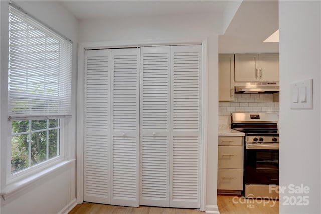 room details featuring electric range, light wood finished floors, light countertops, decorative backsplash, and under cabinet range hood