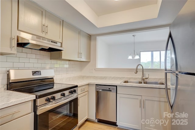 kitchen with light countertops, appliances with stainless steel finishes, under cabinet range hood, and a notable chandelier
