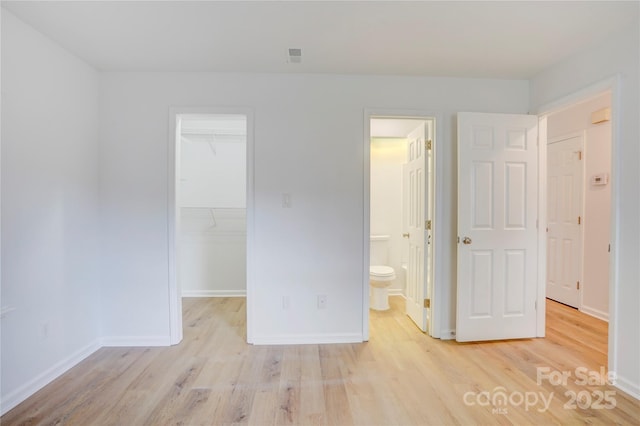 unfurnished bedroom featuring baseboards, a closet, light wood-style flooring, and a spacious closet