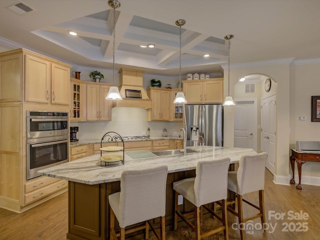 kitchen with appliances with stainless steel finishes, a sink, light brown cabinets, visible vents, and ornamental molding