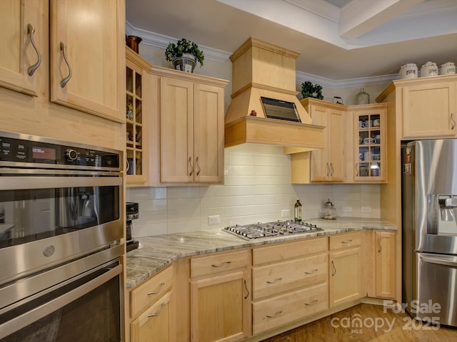 kitchen featuring light brown cabinetry, appliances with stainless steel finishes, decorative backsplash, ornamental molding, and glass insert cabinets
