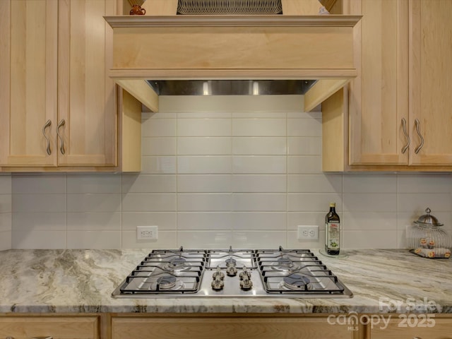kitchen with light brown cabinetry, tasteful backsplash, stainless steel gas cooktop, light stone countertops, and custom range hood