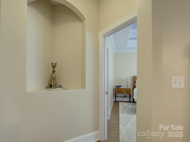 hallway with baseboards, arched walkways, wood finished floors, and ornamental molding