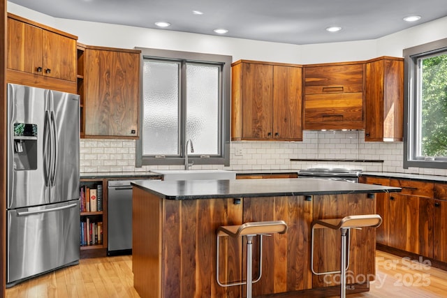 kitchen featuring a kitchen island, dark countertops, a sink, light wood finished floors, and stainless steel appliances