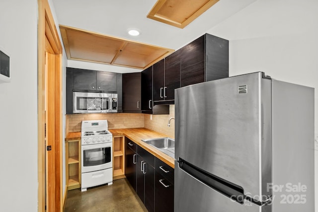 kitchen with concrete flooring, appliances with stainless steel finishes, a sink, dark cabinetry, and decorative backsplash