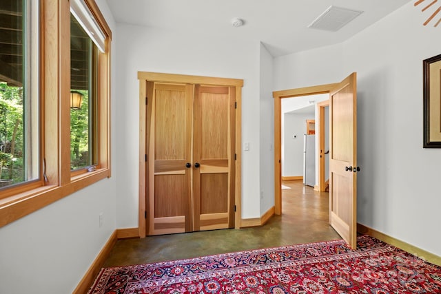 unfurnished bedroom featuring freestanding refrigerator, concrete flooring, baseboards, and visible vents