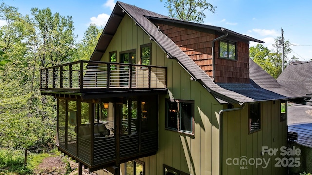 rear view of house featuring board and batten siding, roof with shingles, and a wooden deck