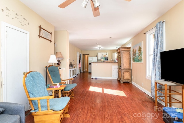 sitting room featuring a ceiling fan, baseboards, and dark wood-type flooring