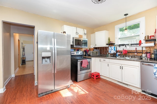 kitchen featuring stainless steel appliances, a sink, light wood-style flooring, and white cabinetry