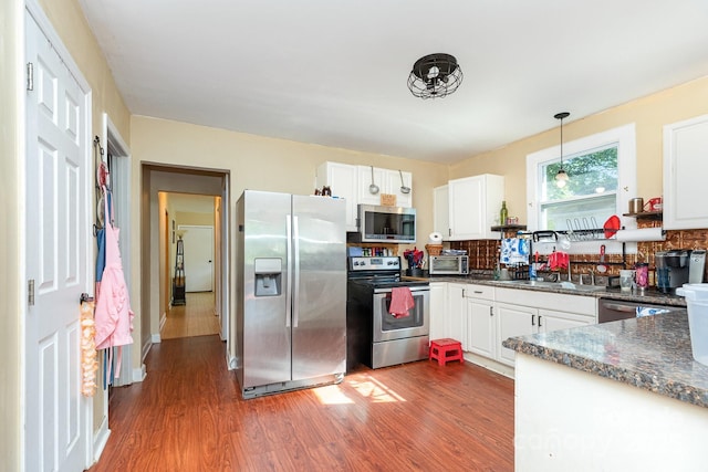 kitchen with stainless steel appliances, dark countertops, dark wood-type flooring, tasteful backsplash, and white cabinetry