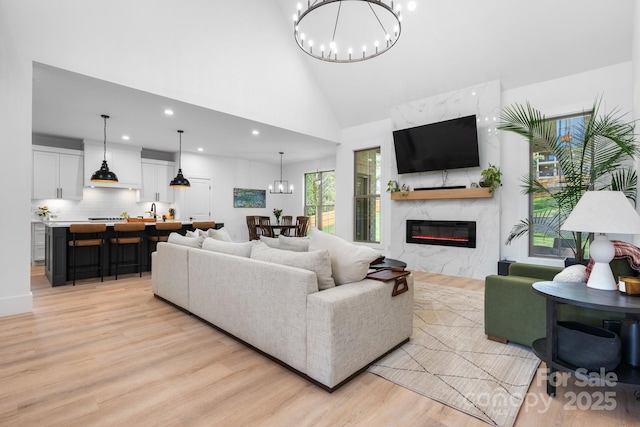 living area featuring a chandelier, high vaulted ceiling, light wood-type flooring, a fireplace, and recessed lighting