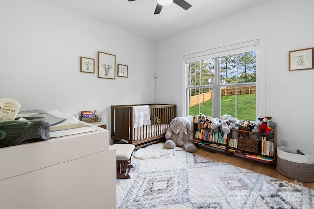 bedroom featuring a crib, wood finished floors, and a ceiling fan