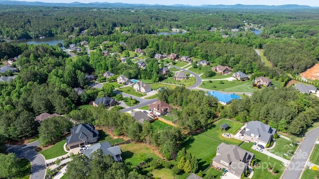 view of property location featuring a heavily wooded area, a nearby body of water, and nearby suburban area