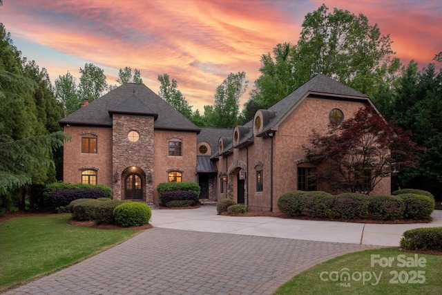 french country style house with curved driveway, stucco siding, a front lawn, and stone siding