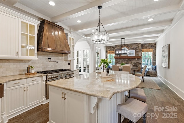 kitchen with dark wood-type flooring, arched walkways, backsplash, stainless steel range, and custom exhaust hood