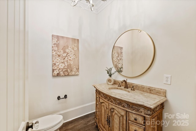 bathroom featuring toilet, wood finished floors, vanity, baseboards, and a notable chandelier
