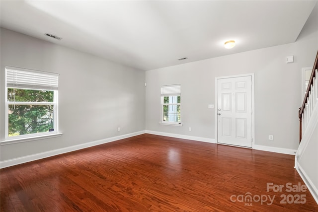 empty room featuring stairs, baseboards, visible vents, and dark wood-type flooring