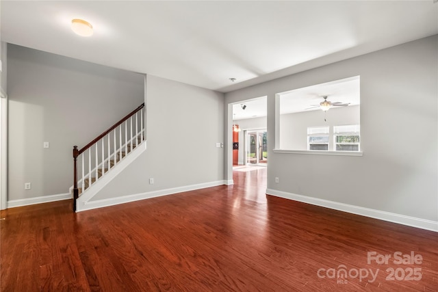 unfurnished living room featuring a ceiling fan, baseboards, wood finished floors, and stairway