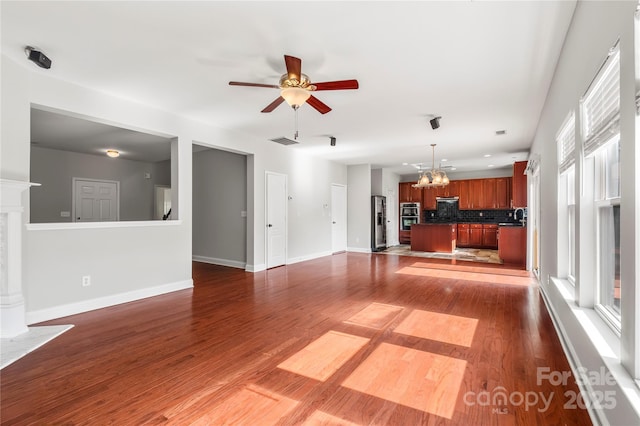 unfurnished living room featuring visible vents, a sink, ceiling fan with notable chandelier, and dark wood-type flooring