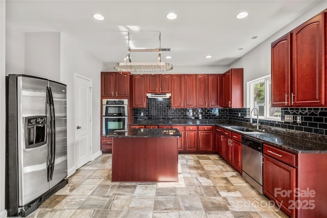 kitchen with a kitchen island, reddish brown cabinets, under cabinet range hood, a sink, and appliances with stainless steel finishes
