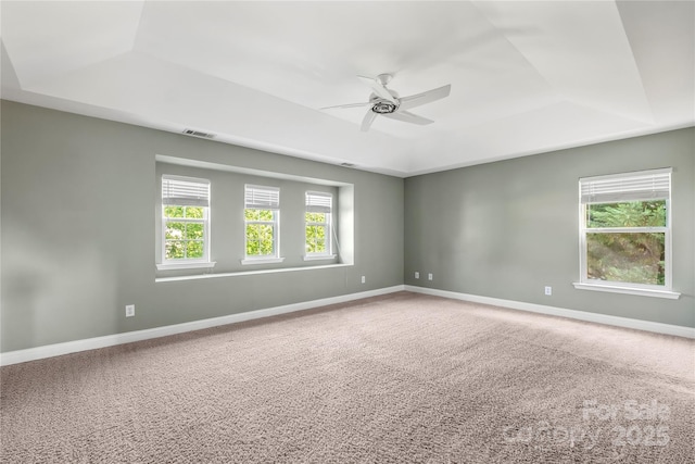 carpeted spare room with visible vents, a ceiling fan, a raised ceiling, and baseboards