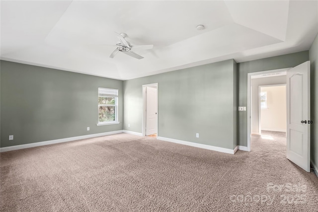 unfurnished room with a raised ceiling, a ceiling fan, baseboards, and carpet