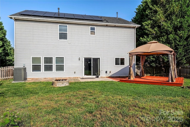 back of property featuring roof mounted solar panels, fence, a gazebo, and a fire pit