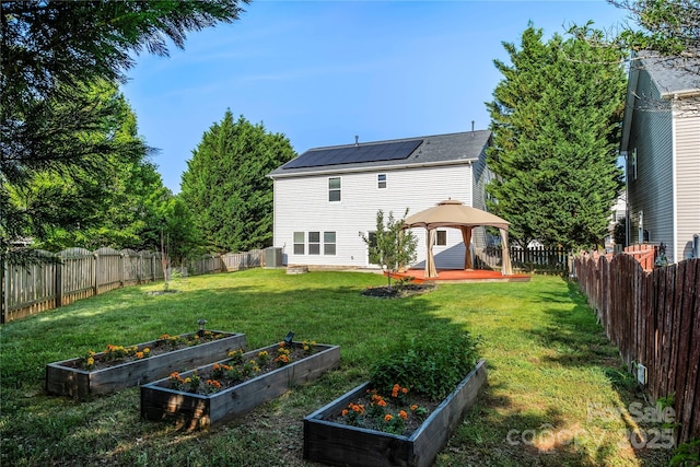 rear view of house with a gazebo, a fenced backyard, a lawn, and a vegetable garden
