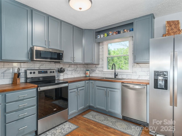 kitchen featuring open shelves, a sink, wood counters, and appliances with stainless steel finishes