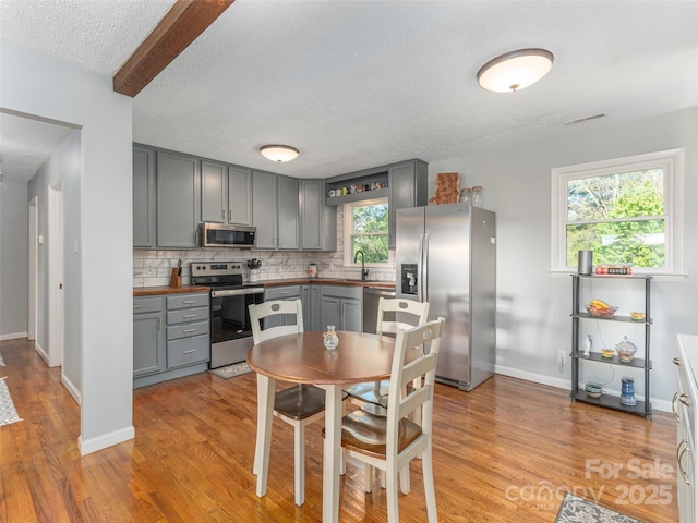 kitchen featuring gray cabinets, appliances with stainless steel finishes, tasteful backsplash, light wood-type flooring, and a sink