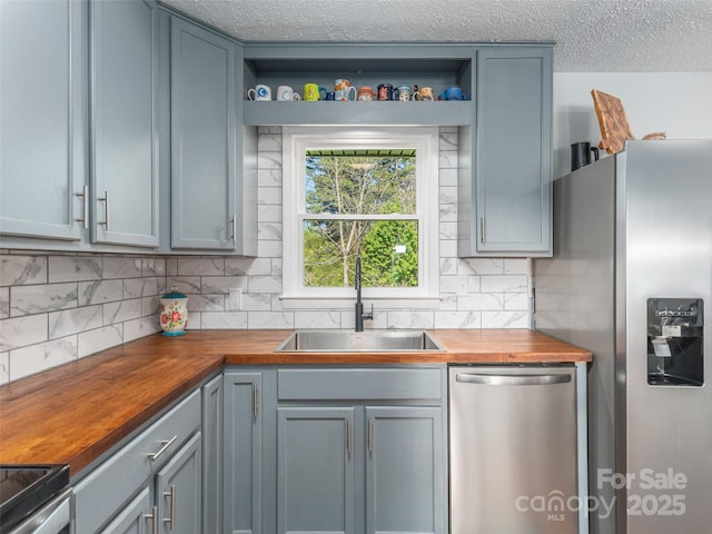 kitchen featuring decorative backsplash, wooden counters, appliances with stainless steel finishes, open shelves, and a sink