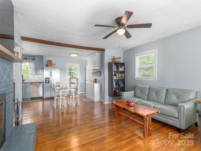 living room featuring ceiling fan, a textured ceiling, a brick fireplace, wood finished floors, and baseboards