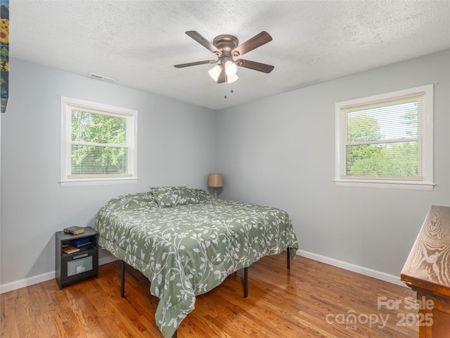 bedroom with visible vents, baseboards, a textured ceiling, and wood finished floors